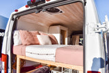 Discover this RV rental's cozy interior, featuring a bed with blush linens, wood ceiling, and clever under-bed storage.