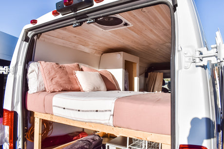 Discover this RV rental's cozy interior, featuring a bed with blush linens, wood ceiling, and clever under-bed storage.