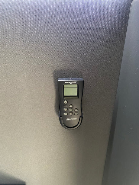 MaxxAir remote control on textured surface, essential for RV rental climate management, with buttons for fan, temp, modes.