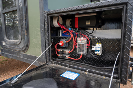 An rv rental's open diamond plate compartment reveals its electrical power system: battery, fuse panel, and wiring.