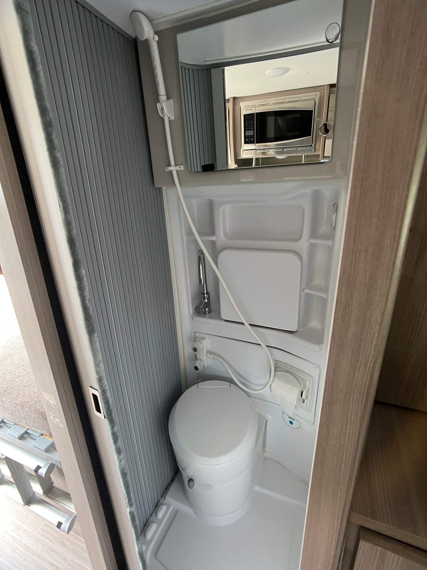 Compact RV rental wet bath, featuring a toilet, shower, sink, and toilet paper holder. A microwave is reflected in the mirror. — photo 12