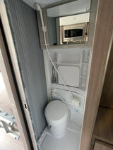 Compact RV rental wet bath, featuring a toilet, shower, sink, and toilet paper holder. A microwave is reflected in the mirror.