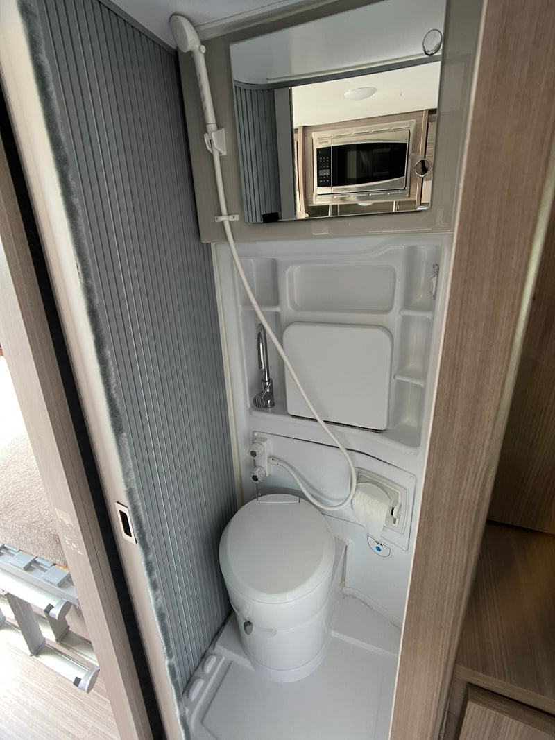 Compact RV rental wet bath, featuring a toilet, shower, sink, and toilet paper holder. A microwave is reflected in the mirror. — photo 12