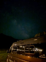 This RV rental is perfectly parked for stargazing! A sleek camper van under a clear night sky, visible Milky Way, and dark hills.