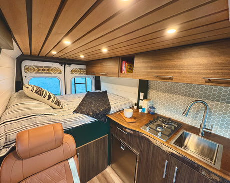 Experience this custom rv rental: features a cozy bed, compact kitchen with wood counters, and lake views.
