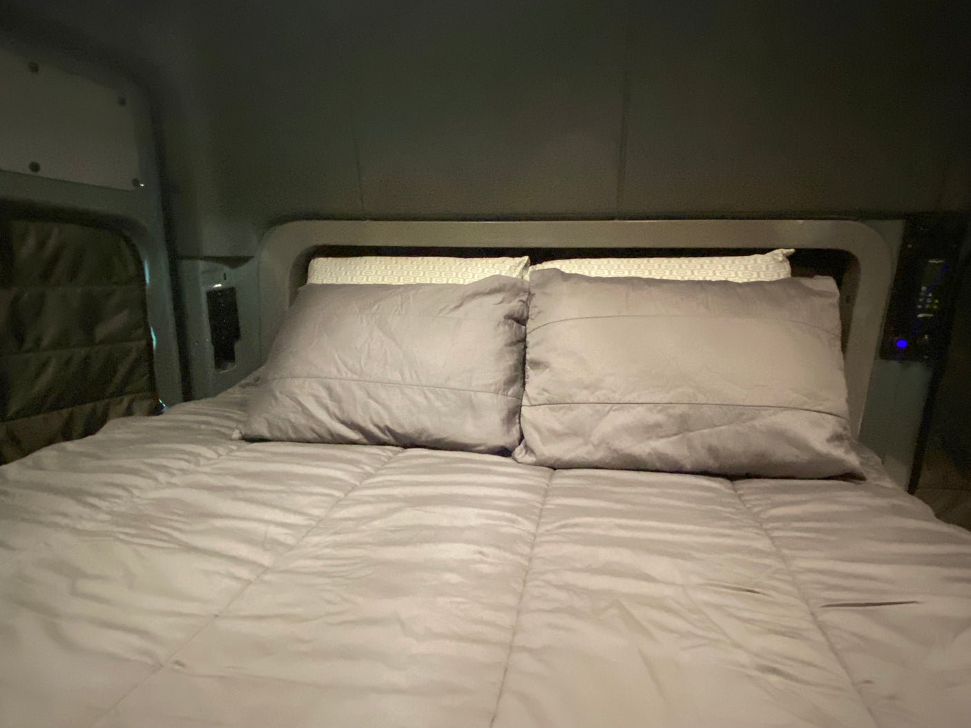 Comfortable grey bed and pillows inside an RV rental. A cozy, compact sleeper space for your travels.