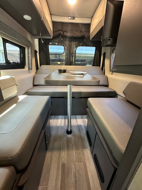 Cozy RV rental interior showing a dinette with a table, bench seats, and overhead storage.