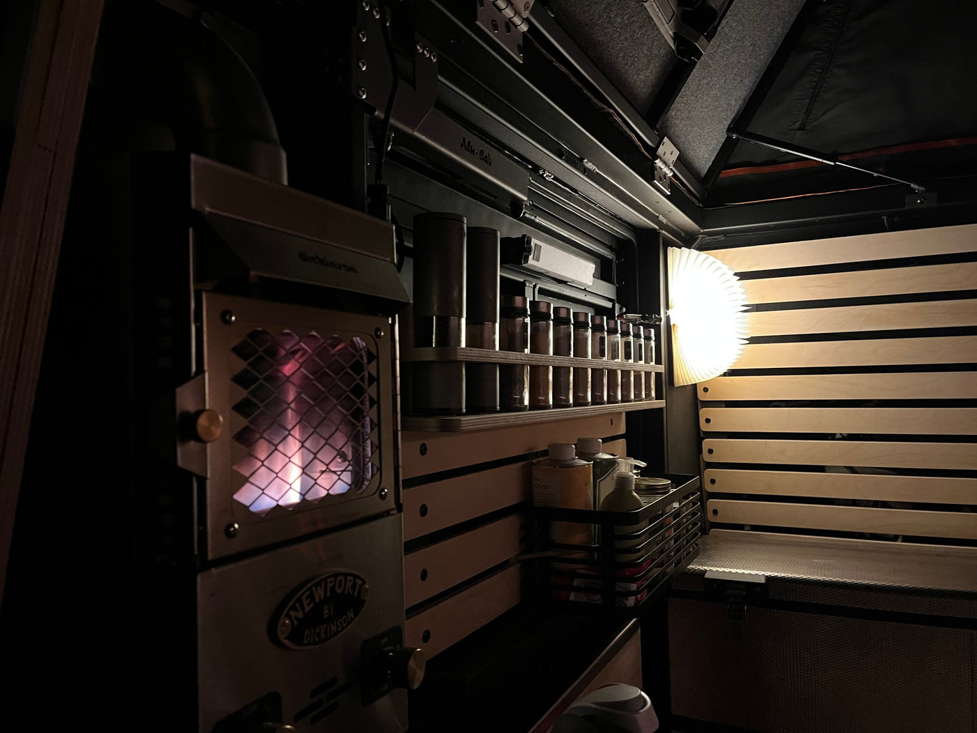 Interior view of an RV rental showing a lit Dickinson Newport heater, spice rack, and soft-glowing lamp. — photo 9