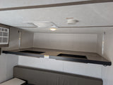 RV rental bunk bed setup in camper interior. Features covered storage bins, AC, and safety devices like a smoke detector.