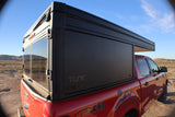 RV rental: Red pickup truck with a black pop-top truck camper. Perfect for off-road adventures and outdoor camping.