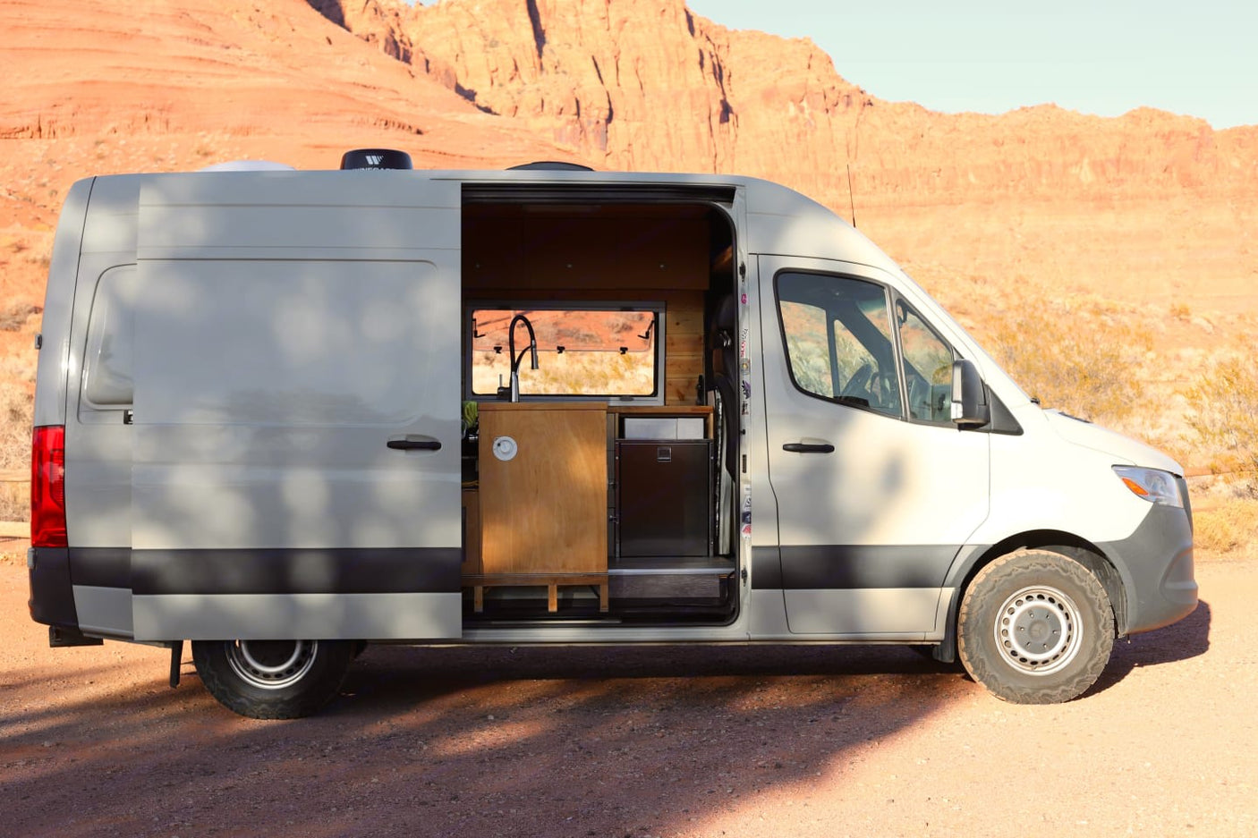 Open-door RV rental camper van with a full kitchen setup in a scenic desert. Ideal for van life adventurers.