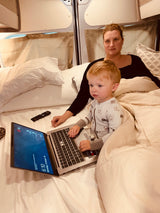 A child and mom use a laptop in their RV rental bed. The screen displays 6:10 AM, Monday, Oct 18.