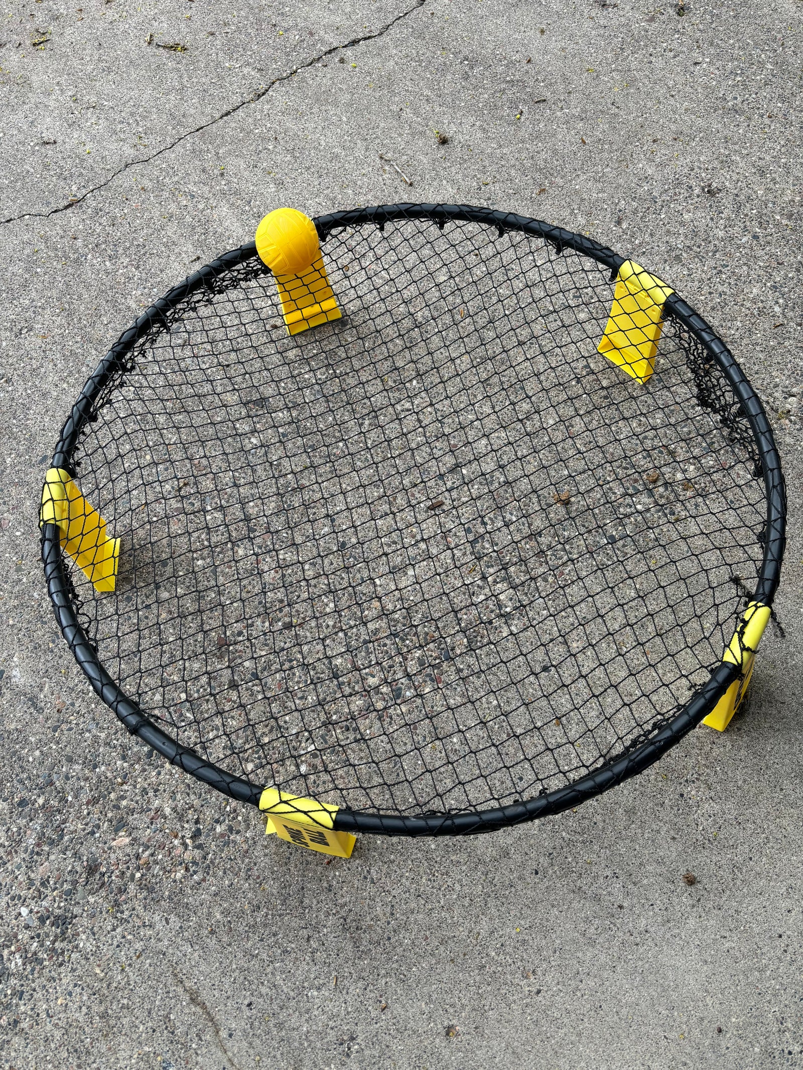 Spikeball set with black net, yellow ball and feet on concrete. Great for outdoor fun on your RV rental trip!