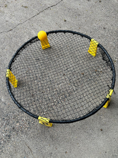 Spikeball set with black net, yellow ball and feet on concrete. Great for outdoor fun on your RV rental trip!