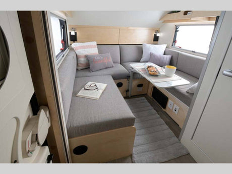 Cozy rv rental interior: a U-shaped dinette with gray cushions, table, book, and rug. Ideal for compact travel.