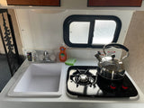 This RV rental offers a compact kitchen with a sink, single-burner stove, kettle, and window, perfect for cooking on the go.