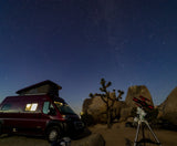 Stargazing in the desert with an RV rental. A pop-top RV and telescope are set among Joshua trees under a starry sky.