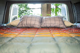 Cozy RV rental bed with open back doors revealing a natural view. Perfect for van life adventures from inside a campervan.