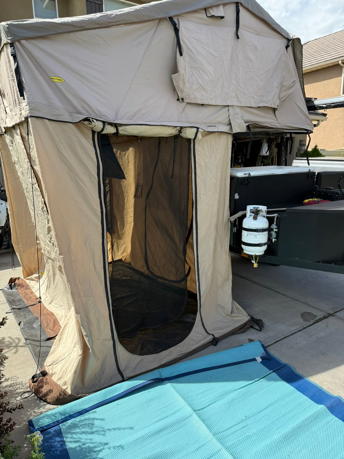  is set up in a scenic mountain area.|An overland RV rental setup with a deployed rooftop tent and awning at an outdoor event on a sunny day. Perfect for camping!|Overland RV rental: Tan Smittybilt rooftop tent with annex — photo 3