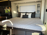Relax in this comfortable RV rental, featuring a cozy bed, modern compact kitchen with a sink, and window views.
