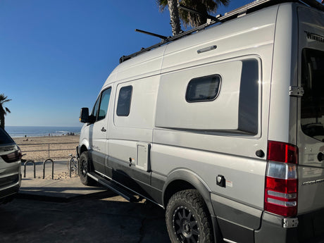 Winnebago Revel RV rental parked oceanside. This grey camper van with a roof rack is ready for beach adventures and van life travel.