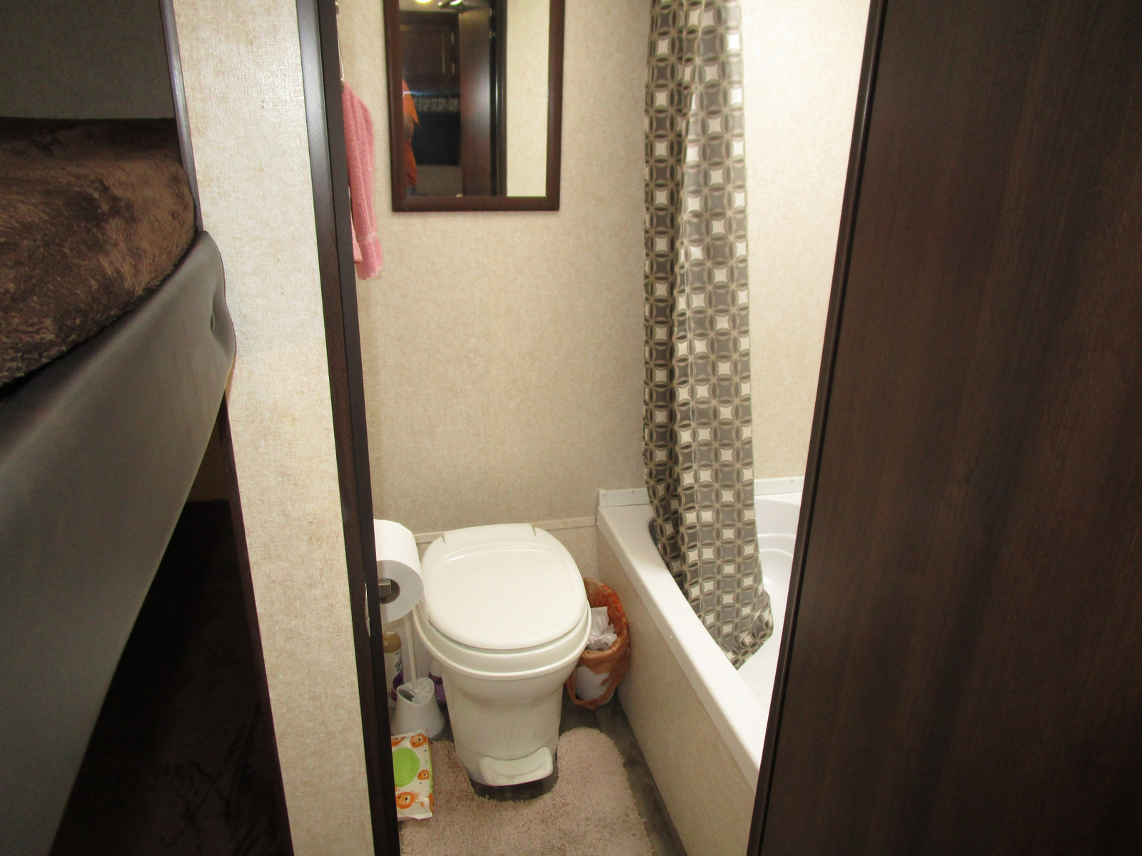 Compact RV rental bathroom features a toilet, shower/tub with curtain, and mirror. Practical and efficient interior for travel.