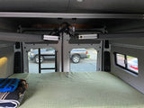 Interior of an RV rental: A comfortable bed fills the rear, with a view through the open back doors and an overhead mounting system.