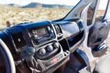Interior of an RV rental camper van, dashboard and open door facing a vast desert with distant mountains.