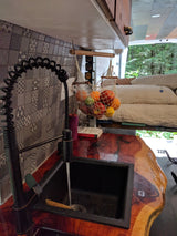 Stylish RV rental kitchen with a black faucet, running water in the sink, live-edge wooden counter, and a hanging fruit net.