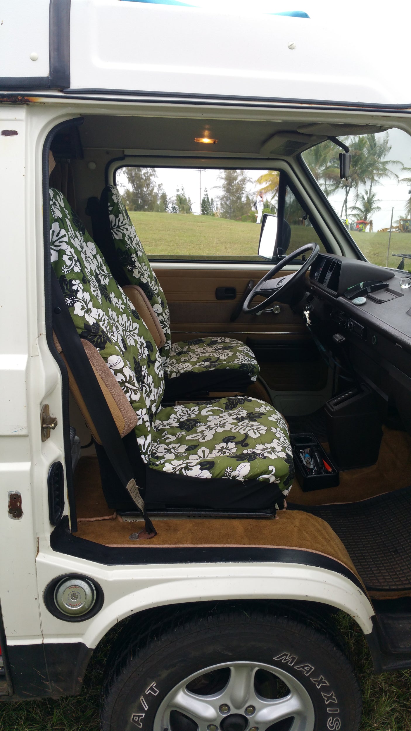 This RV rental's interior features tropical floral seat covers, steering wheel, dashboard, and a view of palm trees outside.
