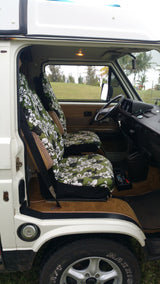 This RV rental's interior features tropical floral seat covers, steering wheel, dashboard, and a view of palm trees outside.