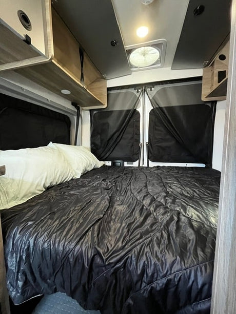 Cozy RV rental interior with a comfy bed, overhead storage, and rear doors, ideal for van life adventures.