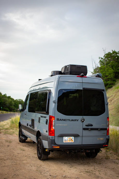 Gray Mercedes-Benz Sprinter Sanctuary RV rental ready for off-road adventure, parked on a dirt road.