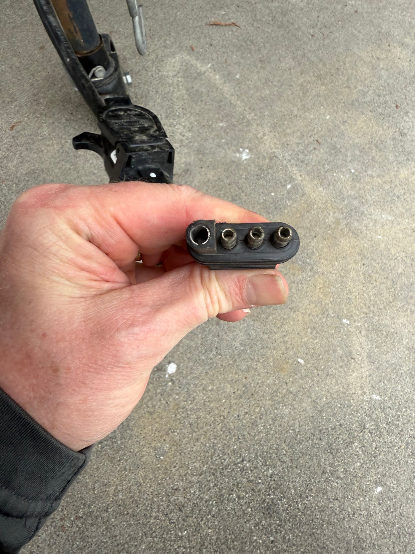 A hand holds a black 4-pin trailer connector (one large, three small holes), vital for RV rental lighting. Hitch in background. — photo 13