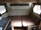 Inside an RV rental, featuring a convertible bed/dinette area, windows with blinds, and a practical kitchen counter.