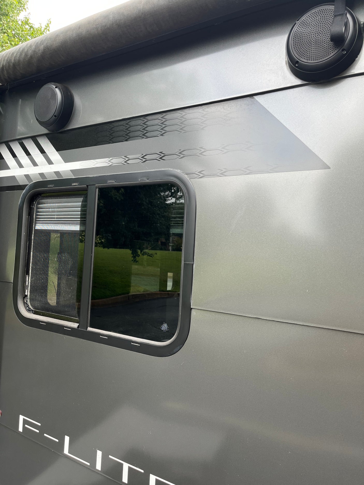 This RV rental's gray exterior features a window, dual outdoor speakers, and decorative honeycomb and stripe decals.
