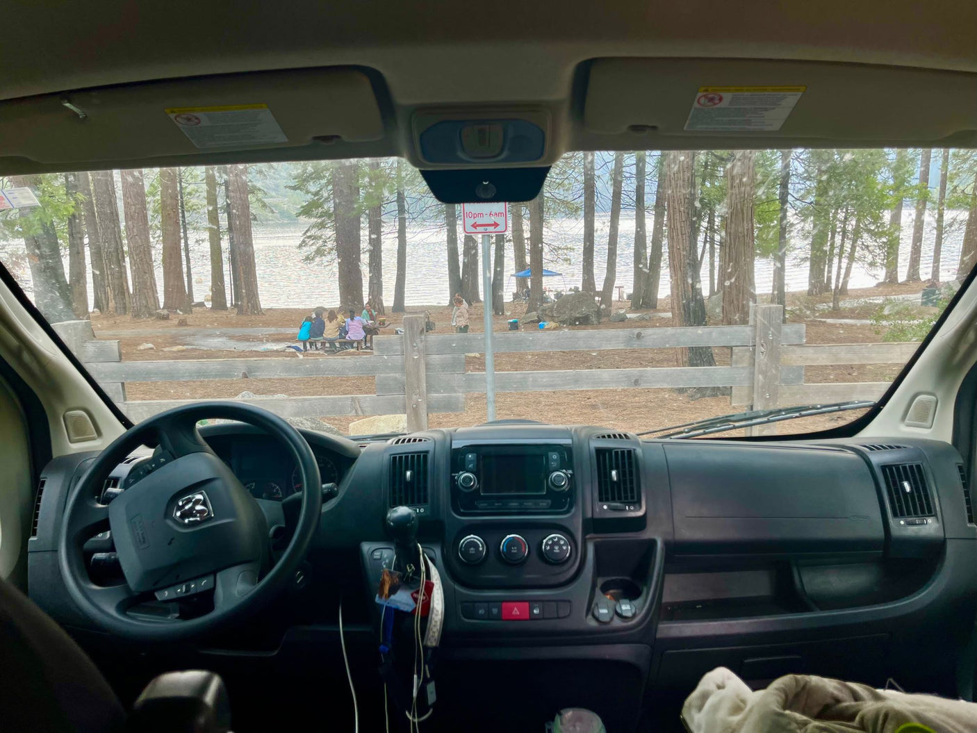 Peaceful lake view from an RV rental. Dashboard and people gathered at a picnic table by the trees.