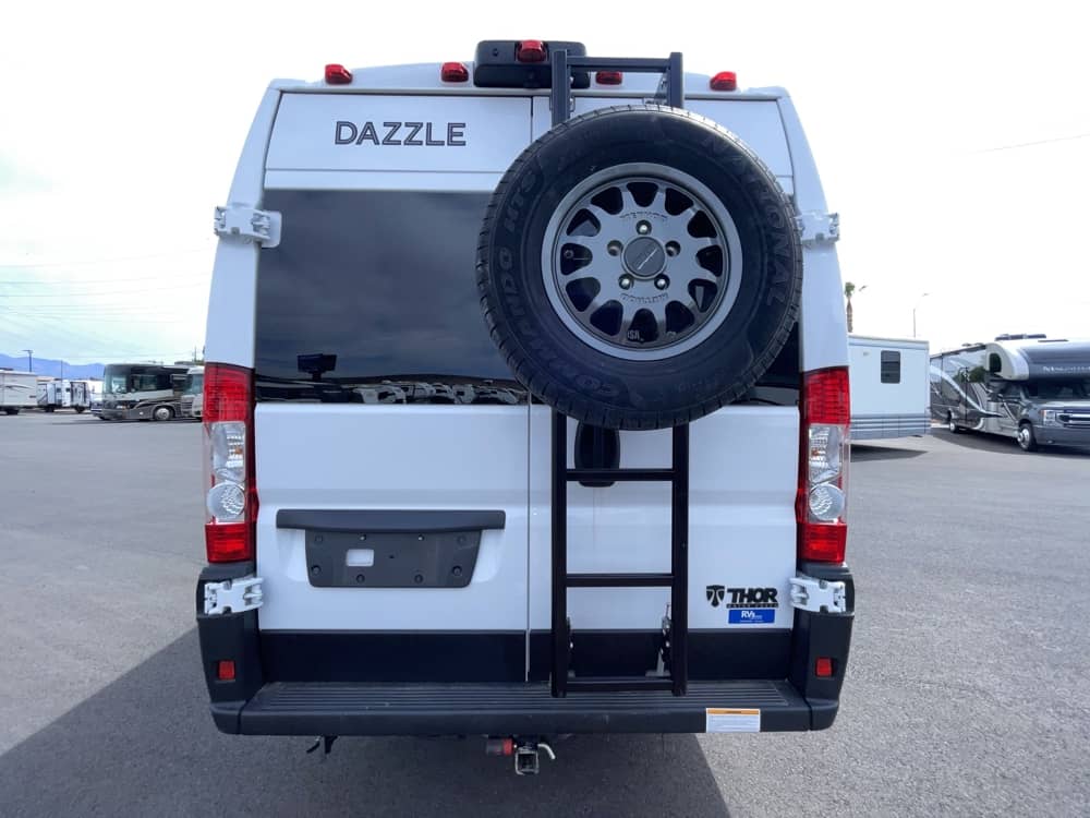Rear view of a white Thor Dazzle RV rental van. It features a spare tire and ladder on the back door.