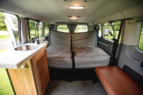 Cozy camper van interior, perfect for an rv rental adventure: bed, kitchenette with sink, and side bench.