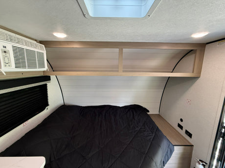 Interior of an RV rental bedroom showing a bed, AC unit, overhead cabinets, and skylight. Ready for your next adventure.