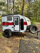 White and red Sunray Sport teardrop RV rental, ready for off-grid camping. Parked by trees on a sunny day.