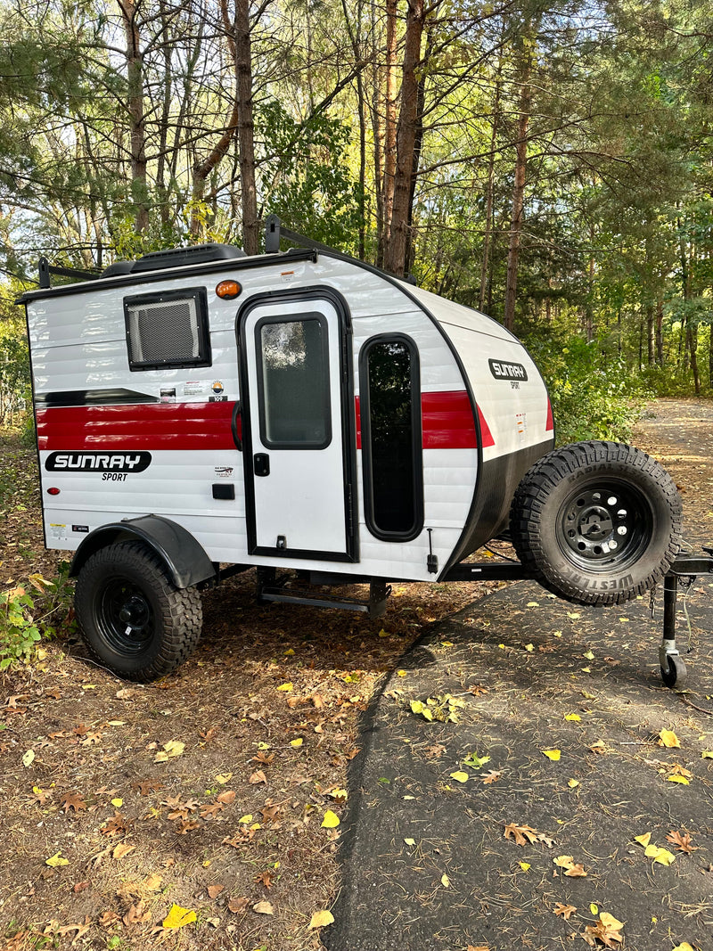 White and red Sunray Sport teardrop RV rental, ready for off-grid camping. Parked by trees on a sunny day. — photo 12