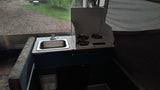 Pop-up RV rental interior: compact kitchen with sink, three-burner stove, and a view of the gravel outside.