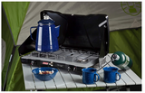 Perfect for RV rental trips: a Coleman camping stove with coffee percolator, mugs, and bowl on a table by a tent.