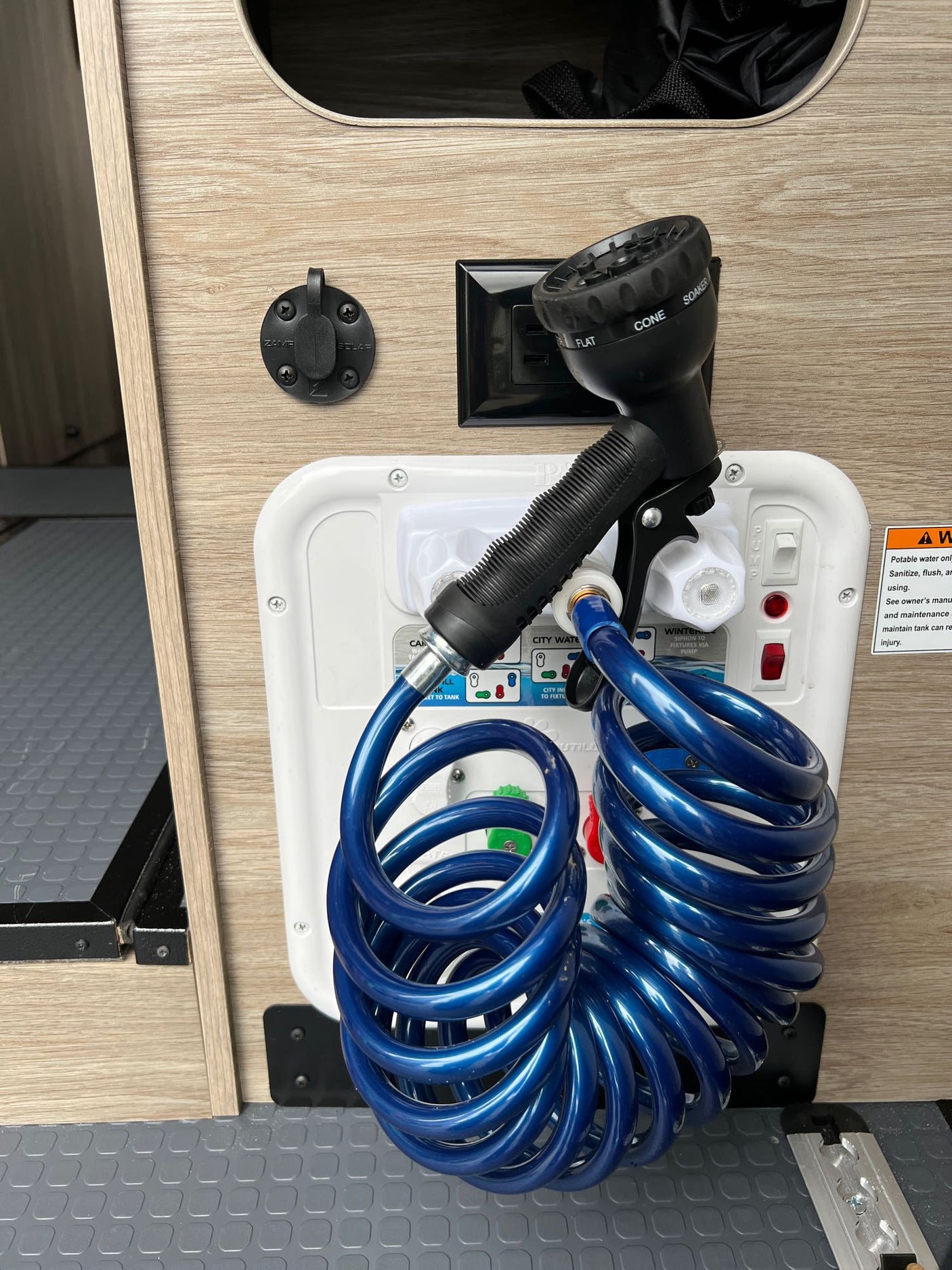 RV rental's water panel with a blue coiled shower hose, sprayer, water controls, and a Zamp Solar charging port.