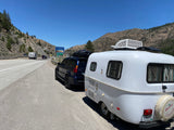 White Scamp rv rental and Lexus SUV parked on a Nevada highway next to the state sign, ready for mountain adventures.