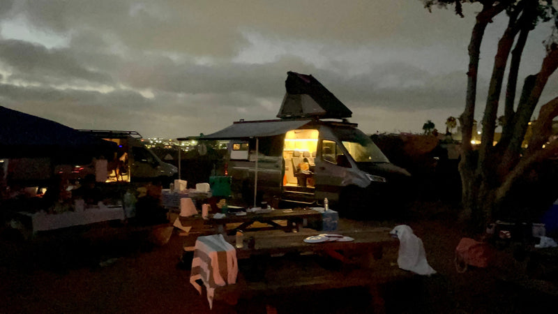  ideal for RV rental. Night scene shows the van parked on a street by a lit fence.|Custom RV rental: A Sprinter van with a rooftop tent and awning — photo 12