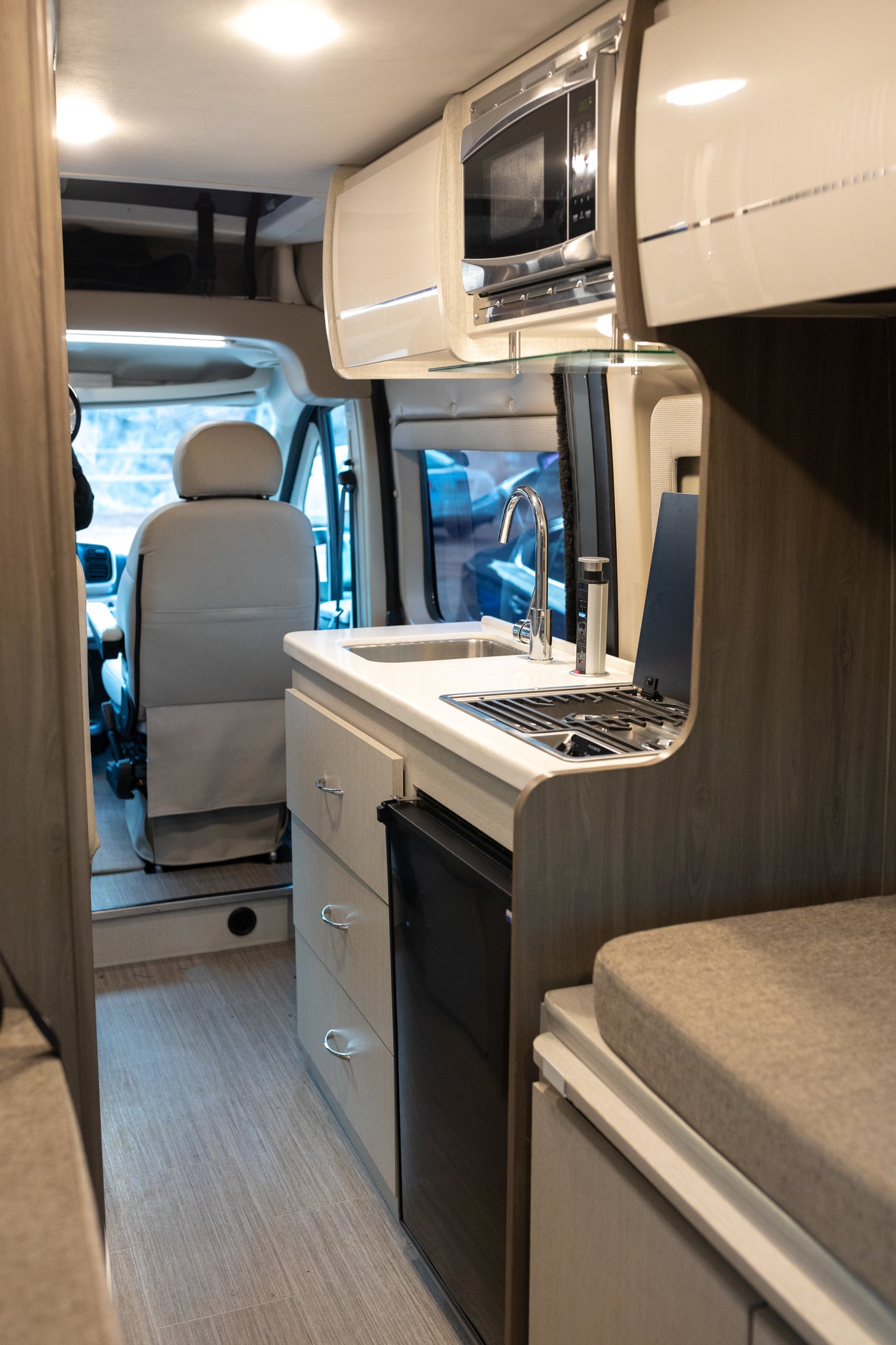 RV rental's galley features a sink, stove, microwave, and fridge, looking towards the driver's cab.