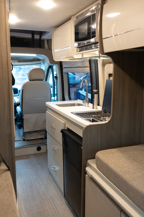 RV rental's galley features a sink, stove, microwave, and fridge, looking towards the driver's cab.