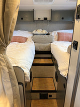 A well-appointed RV rental bedroom with two comfortable twin beds, steps, and convenient overhead storage.